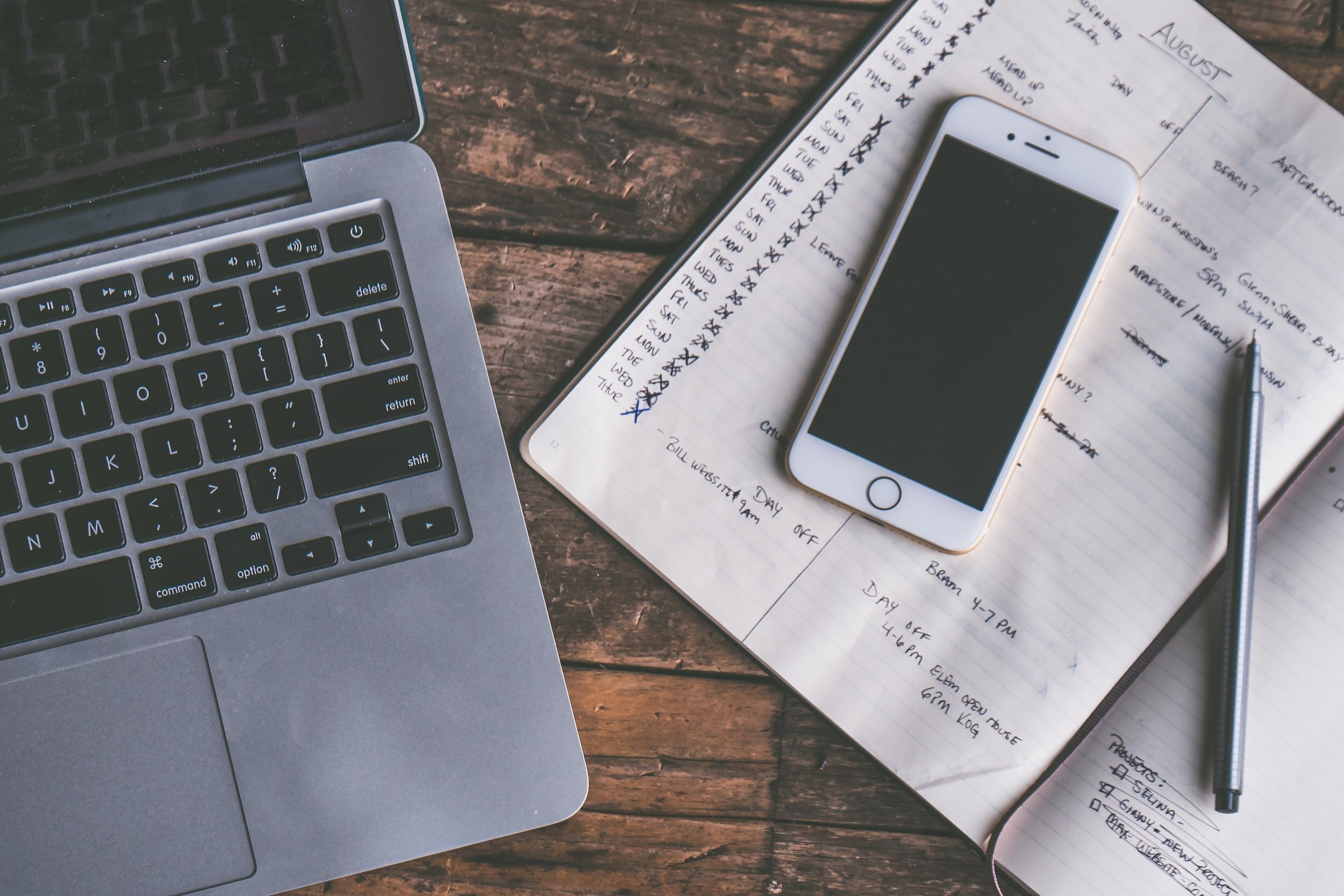 Laptop, phone, and notebook on a wooden desktop